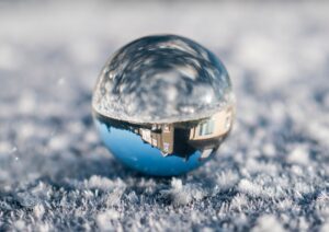 A glass orb reflecting the sky and a house. The ground which the orb sits on is frosty.