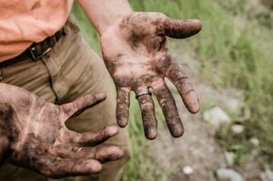 A man shows his hands covered in mud and soil.